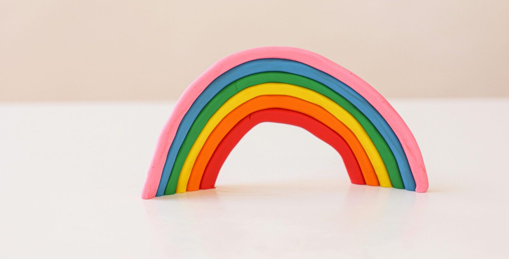 retrouver sa lumière A vibrant clay rainbow sculpture on a white background, showcasing a minimalistic art piece.